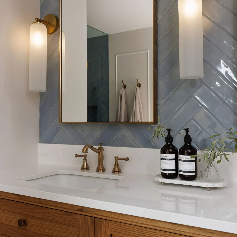 Ensuite oak vanity with brass-framed mirror, frosted glass sconces, blue herringbone tile and aged brass faucet, Ten Mile Point renovation by Maverick Design, Victoria BC