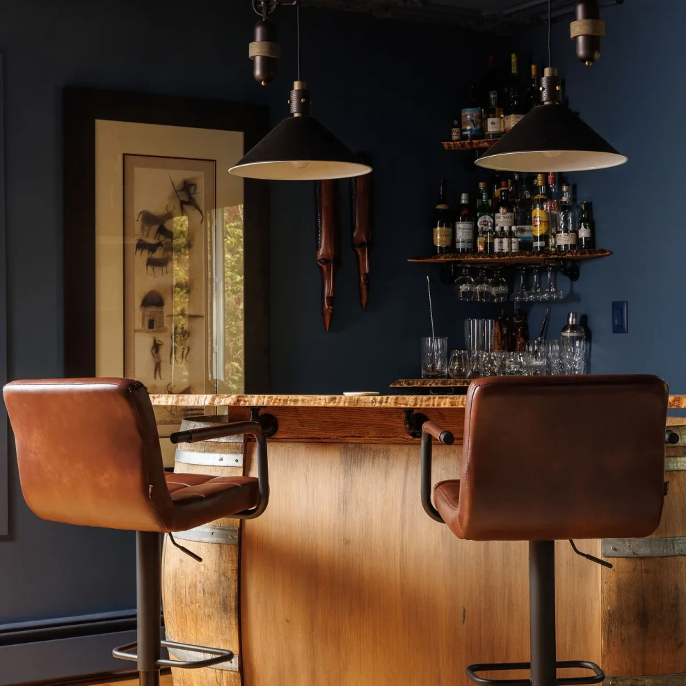 Games room bar with wine barrel base, live-edge top, leather stools and pulley pendants under a navy coffered ceiling, 10 Mile Point renovation by Maverick Design, Victoria BC