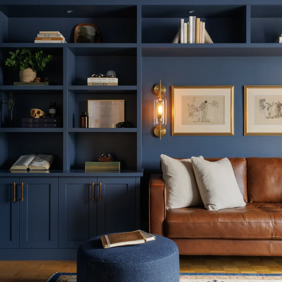 Colour-drenched navy home office with built-in shelving, brass sconces and cognac leather sofa, Ten Mile Point renovation by Maverick Design, Victoria BC